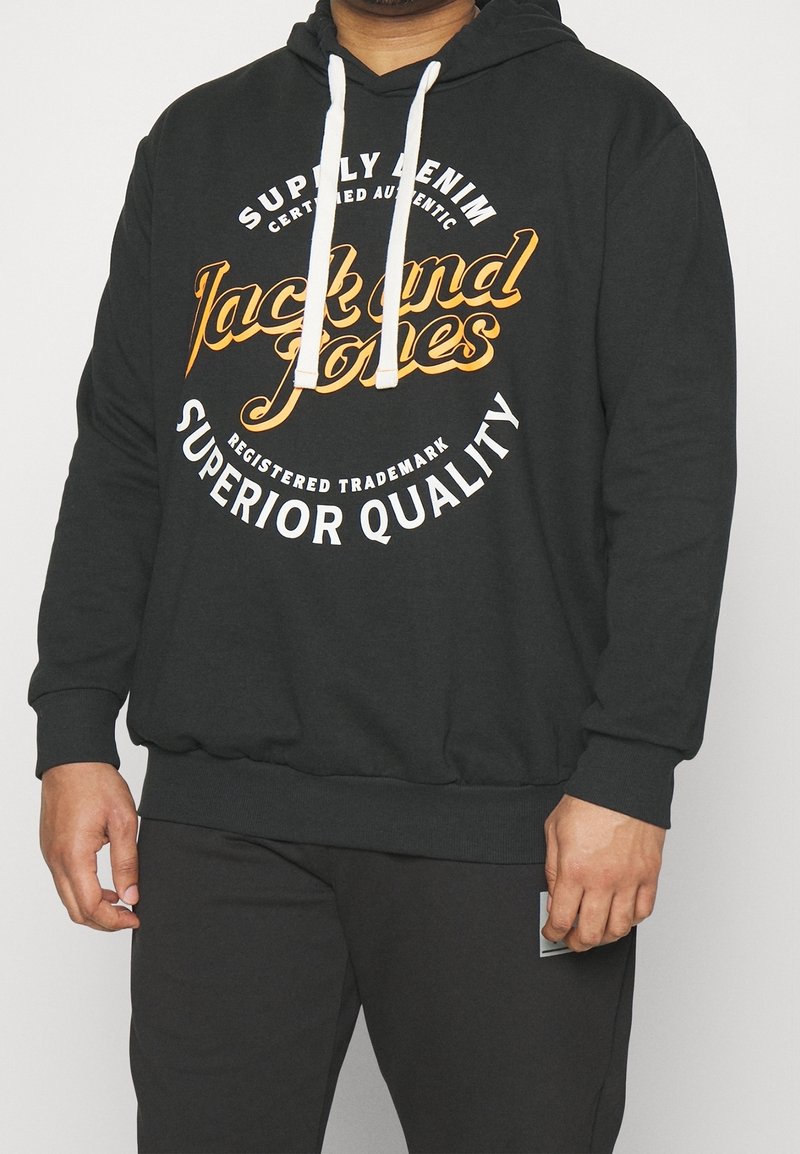 Svart sweatshirt med dragsko, med en stor grafik i orange och vit text. Ribbad mudd och nederkant, tillverkad av mjukt material.