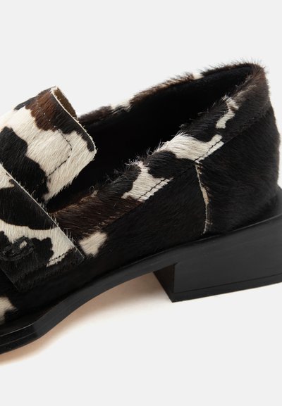 Čiernobiela mokasína s textúrou kozej kože, nízkym blokovým podpätkom a detailom popruhu cez prednú časť, zobrazená z bočného uhla na bielom pozadí.