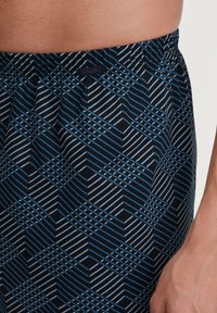 Zwarte en blauwe boxers met geometrische patronen. Gemaakt van zachte stof, met een elastische tailleband en een klein logo-label.
