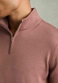 Pullover morbido color rosa con colletto a metà zip. Il tessuto è liscio ed elastico, con una texture a coste pulita.