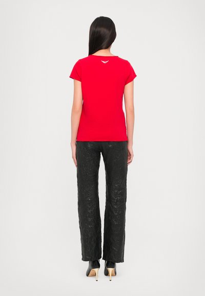 Red fitted t-shirt with short sleeves and a subtle white logo on the back, paired with crinkled black wide-leg trousers and black heels.