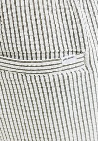 Tissu blanc avec fines rayures verticales noires et une poche arrière arborant une petite étiquette "JACK & JONES".