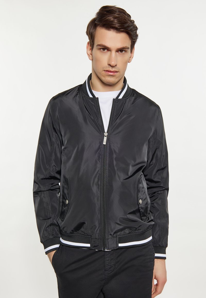 Giubbotto bomber nero con una texture liscia e lucida, polsini e vita a coste rigate, con zip frontale e due tasche laterali.