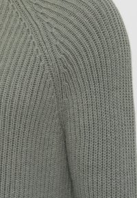 Gaiši zaļš adīts džemperis ar ribotu faktūru. Iekļauj apaļu plecu šuvīti un vertikālu rakstu. Mīksts, vidējas svara audums.