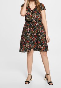 Svart klänning med korta ärmar och V-ringning, med ett blommönster i rött, rosa och grönt. Knut vid midjan, över knä-längd.