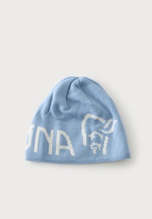 Bonnet tricoté bleu clair avec un visage blanc stylisé et un texte partiel sur le bord, posé à plat sur un fond clair uni.