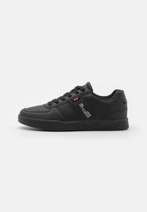 Black athletic sneaker with a smooth leather upper, round toe, contrasting white stitching, and a textured rubber sole. Features lace-up design.