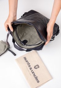 Zwarte leren rugzak met een ritssluiting. Het interieur heeft een gestructureerde beige voering en organisatiezakken. Inclusief een stoffen stofzak.