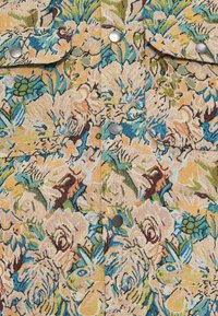 Floral-patterned fabric featuring peach and blue hues, textured weave, with silver metal snap fasteners and dual chest pockets.