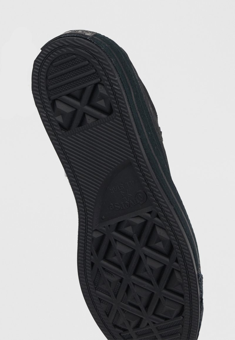 Black sneaker sole with textured geometric patterns and grooves, showing tread design and brand logo on the bottom.