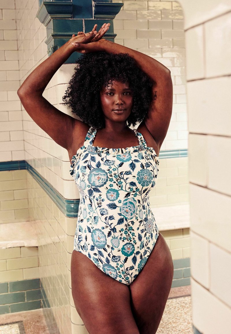 Virágmintás, egyrészes fürdőruha fehér alapon, kék virágmintázattal. Ráncos pántokkal és testhezálló fazonnal rendelkezik.