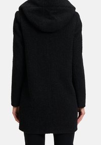 Cappotto nero con cappuccio realizzato in un tessuto mélange testurizzato. Presenta un design a taglio dritto e maniche lunghe, che si estendono fino a metà coscia.
