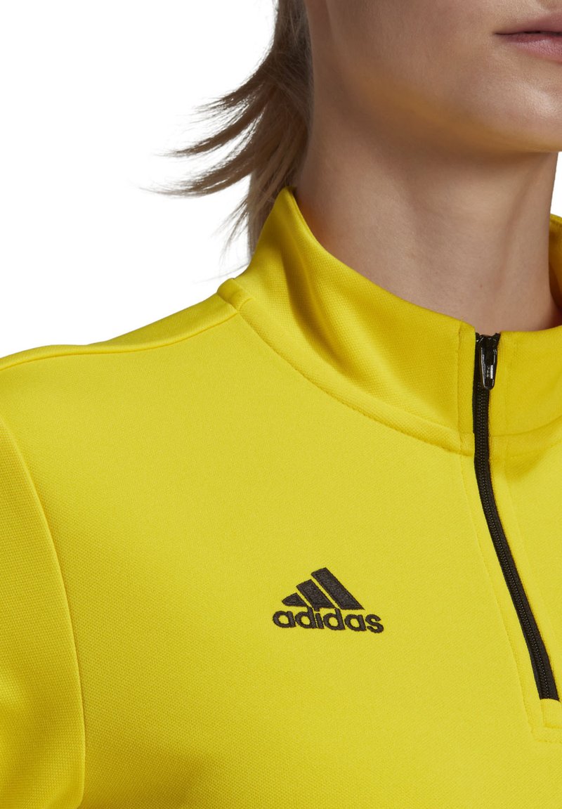 Giacca sportiva gialla con collo a zip, realizzata in materiale liscio, con il logo Adidas nero sul lato sinistro superiore.