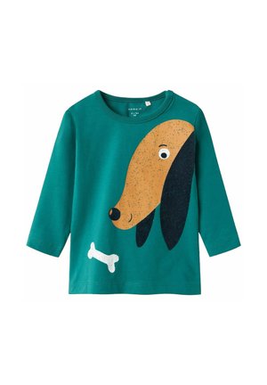 Camiseta de manga larga color verde azulado con la imagen de una cara de perro de dibujos animados en diseño marrón y negro, acompañada de un gráfico de un hueso blanco en la parte inferior.