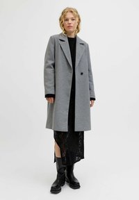 Manteau en laine mélangée gris avec des revers notés et une fermeture à un bouton, associé à une robe en dentelle noire et des bottes noires jusqu'aux genoux.