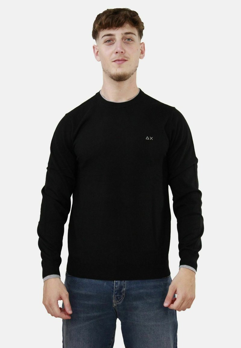 Maglione nero a maniche lunghe con scollatura rotonda, realizzato in materiale morbido. Presenta un piccolo logo sul lato sinistro del petto e polsini a coste.