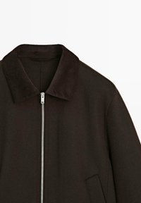 Giacca marrone scuro con colletto in corduroy, chiusura frontale con zip e tasche laterali; realizzata in tessuto liscio, con linee pulite e design minimale.