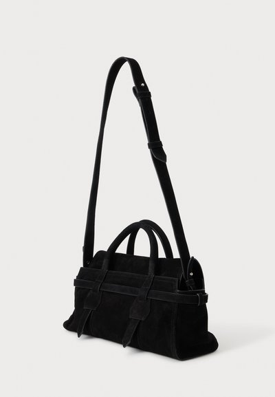 Sac à main en daim noir avec deux petites anses et une longue bandoulière réglable sur un fond clair uni.