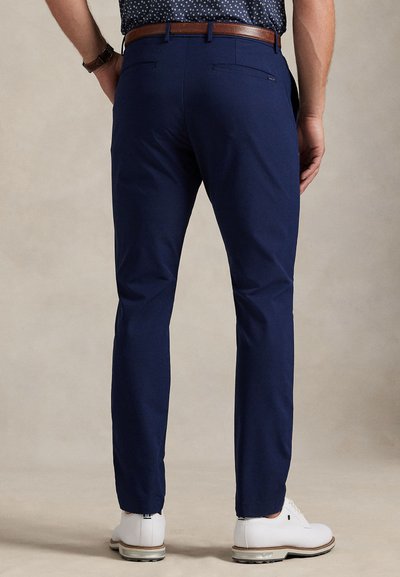 Σκούρο μπλε παντελόνια σε στενή γραμμή, με θηλιές για ζώνη και δύο πίσω τσέπες, συνδυασμένα με λευκά παπούτσια. Λείο ύφασμα και ραμμένο σχέδιο.