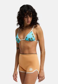 Σετ μαγιό δύο τεμαχίων που περιλαμβάνει τοπ μπικίνι τρίγωνο σε ανοιχτό μπλε με πράσινο λουλουδάτο μοτίβο και σορτς με ψηλή μέση σε ροδακινί χρώμα με λευκή λεπτομέρεια.