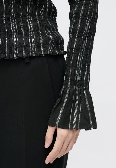 Top negru cu textură și dungi verticale argintii, cu detalii adunate și mâneci evazate. Asortat cu pantaloni negri conici.