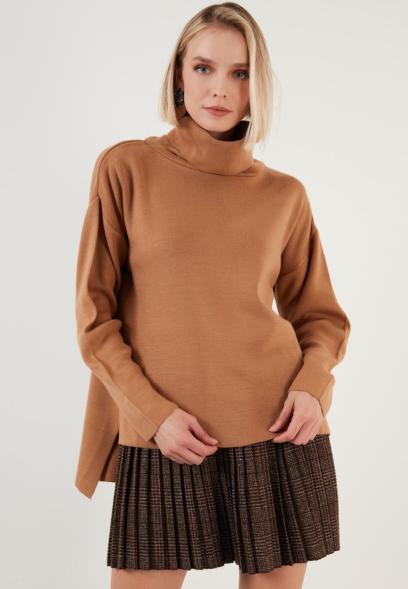 Brauner Rollkragenpullover mit langen Ärmeln; weicher Strickstoff. Kombiniert mit einem braunen karierten Faltenrock, der kontrastierende Muster und Farben zeigt.