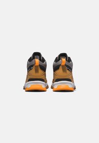 Rückansicht von braunen und schwarzen Sneakers mit orangefarbenen Akzenten, die eine strukturierte Oberfläche, einen gepolsterten Schaft und eine gemusterte Sohle für guten Grip bieten.