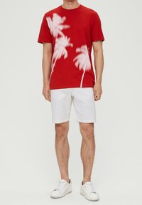 T-shirt rouge en coton avec des motifs de palmiers blancs, associé à un short blanc et des baskets blanches. Design simple avec un col rond.