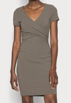 Frau trägt ein kurzärmeliges, geripptes Wickelkleid in Taupe mit V-Ausschnitt, figurbetonter Taille und knielangem Saum vor einem einfarbigen Hintergrund.