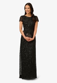 Abito da sera nero di paillettes con maniche corte, silhouette aderente e uno spacco laterale. Accompagnato da una piccola pochette nera.