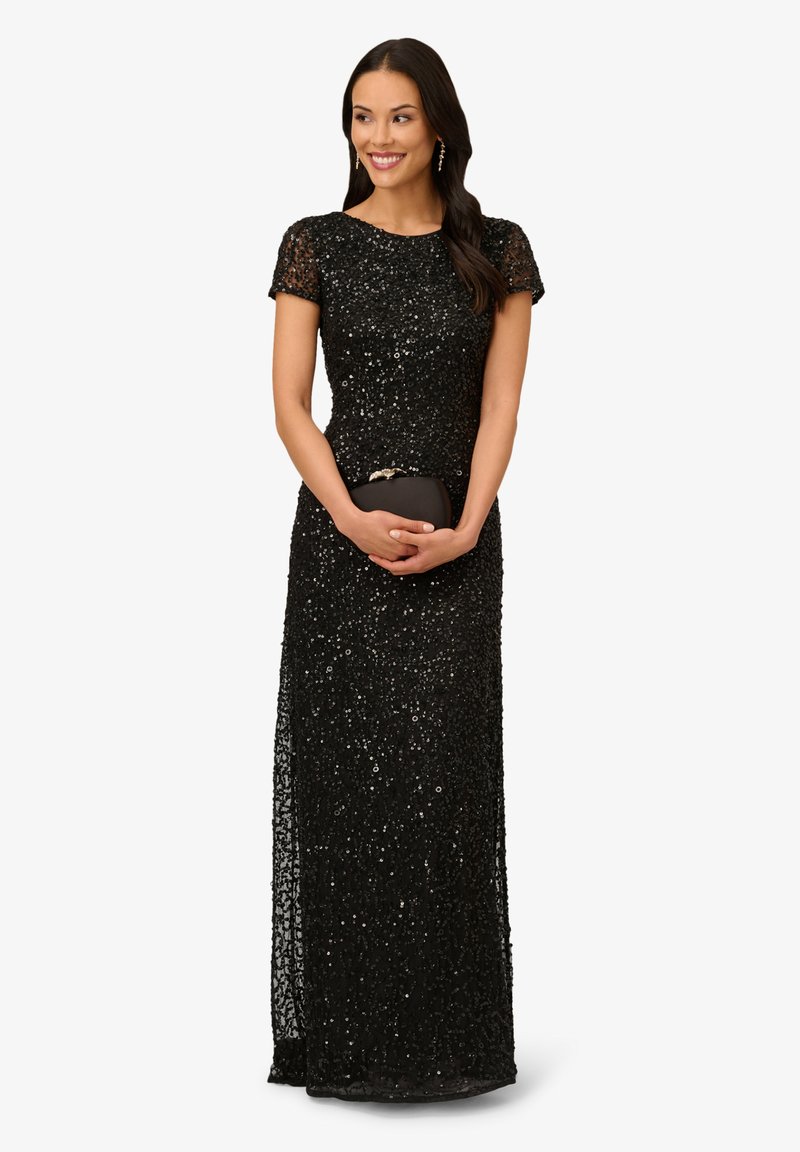 Abito da sera nero di paillettes con maniche corte, silhouette aderente e uno spacco laterale. Accompagnato da una piccola pochette nera.