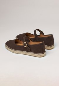 Brązowe zamszowe espadryle na płaskim obcasie z zapięciem na klamrę, o zaokrąglonym czubku i wyplatanej podeszwie z juty. Gładka tekstura i prosty design.