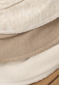 Tres capas de tela en tonos beige, con texturas suaves, una superficie ligeramente arrugada y costuras visibles a lo largo de los bordes.