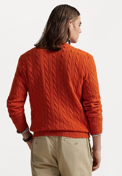 Pull en maille côtelée orange avec ourlet et poignets côtes, présentant un motif texturé. Porté par-dessus une chemise à col bleu clair, vue de dos.