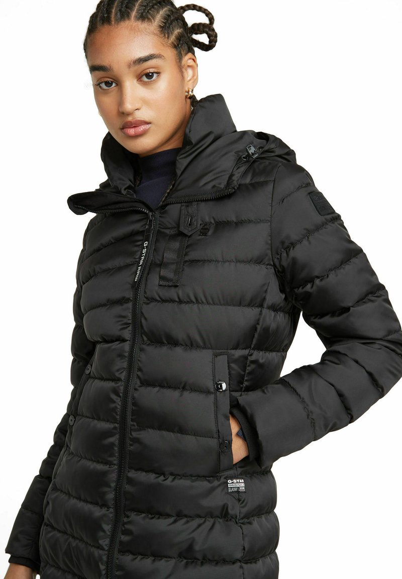 Schwarze Puffy-Jacke mit hohem Kragen, Reißverschluss und gerippten Bündchen. Verfügt über horizontale Nähte und ein Logopatch auf dem Ärmel.