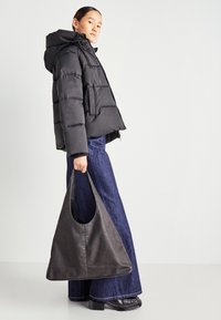 Black puffer jacket with hood, zip closure, and front pocket; paired with high-waisted, wide-leg dark denim pants and a large black tote bag.