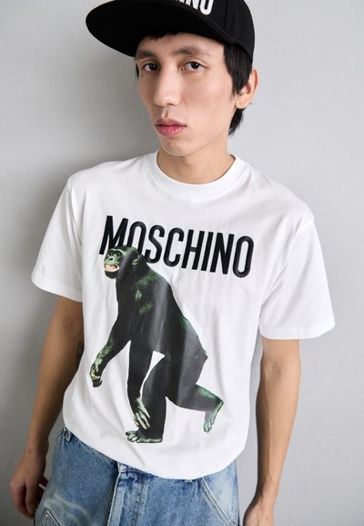 Hvid bomulds t-shirt med et stort grafisk motiv af en sort abe og ordet "MOSCHINO" i fede sorte bogstaver ovenfor designet.