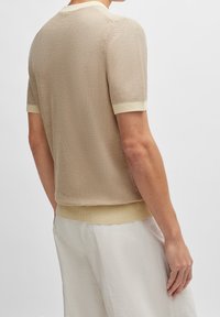 Pull en maille à manches courtes beige clair avec tissu texturé et bordure contrastante crème aux poignets et à l'ourlet inférieur. Design minimaliste.