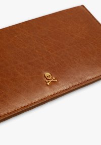 Billetera de cuero marrón con un acabado texturizado y un acento dorado de calavera y tibias cruzadas. Presenta bordes limpios y rectos, y costuras visibles.