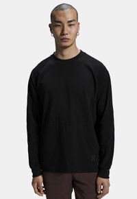 Felpa nera a maniche lunghe con maniche raglan e un dettaglio della cucitura frontale. Realizzata in tessuto liscio con un logo discreto vicino all'orlo.