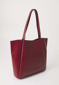 Burgunderfarget totebag laget av strukturert syntetisk lær, med høye håndtak og en glatt tekstur, samt en flat lomme på forsiden.