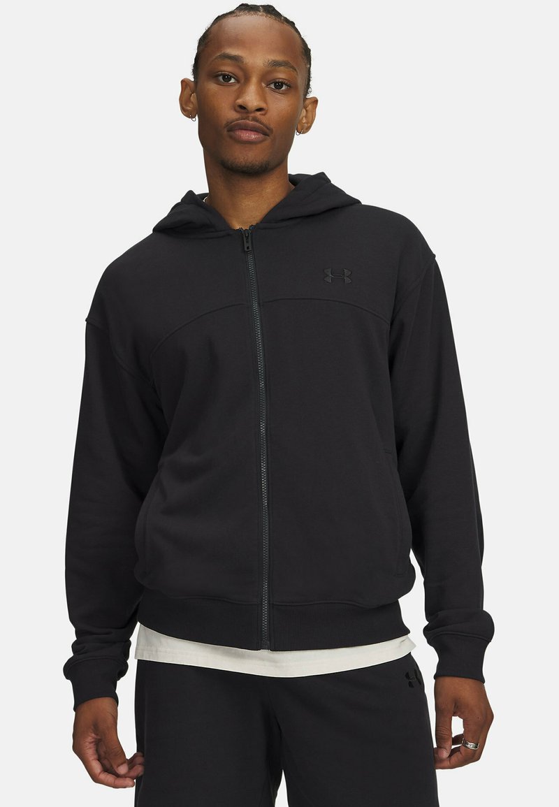 Sweat à capuche noir zippé fabriqué en tissu doux, avec une capuche, des poches avant et un logo discret sur la poitrine. Assorti à un pantalon foncé.