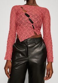 Pink lace long-sleeve top with a cut-out design, featuring a textured pattern. Paired with fitted black leather trousers.