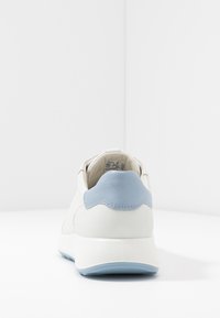 Sneaker bianca in pelle con un accento blu chiaro sul tallone. Texture liscia, forma arrotondata e design minimalista con dettagli di cucitura.