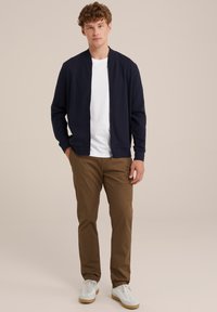 Marineblaue Bomberjacke aus strukturiertem Stoff, weißes T-Shirt, khakifarbene Hose und weiße Sneakers. Einfaches, lässiges Design mit Reißverschluss.