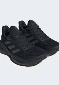 Czarne buty sportowe z przewiewną siateczką, grubą gumową podeszwą i trzema tonowanymi paskami po bokach. Lekką konstrukcję z sznurowadłami.