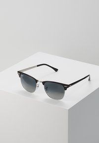 Ochelari negri cu lentile gri degradat, accente metalice și brațe din plastic elegante. Designul are o formă modernă de tip cat-eye.