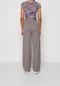 Grijze wijde broek van een gladde stof, gecombineerd met een aansluitend, tie-dye T-shirt met korte mouwen in verschillende tinten blauw en grijs.
