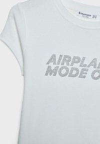 Valkoinen puuvillahuppari, jossa on lyhyet hihat, ja johon on kirjailtu teksti "AIRPLANE MODE ON" hopeisilla strasseilla. Pinta on sileä.