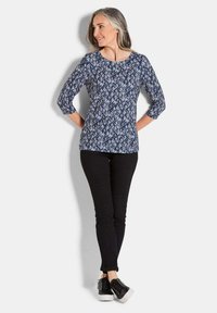 Blauwe gebloemde top met een ronde halslijn en driekwartmouwen, gecombineerd met zwarte slim-fit broek en zwarte sneakers met witte zolen.